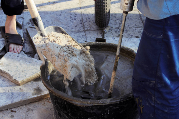 Trabajador están mezclando cemento con una herramienta un mezclador de construcción para la fijación de las baldosas de revestimiento durante la reparación del porche del cine
. - Foto, Imagen