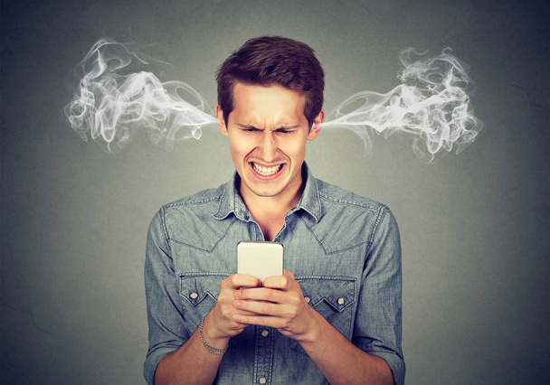 Angry man reading a text message on smartphone blowing steam coming out of ears  - Foto, Imagem