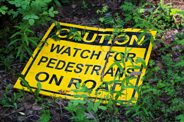 A caution watch for pedestrians on the road sign laying on the ground - Photo, Image