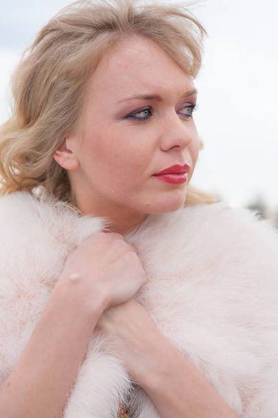 Young blond woman in a beige dress and a short pink fur coat on the countryside road - Foto, Imagem