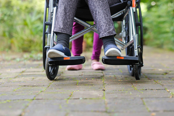літня жінка в інвалідному візку, що йде з доглядальницею
 - Фото, зображення