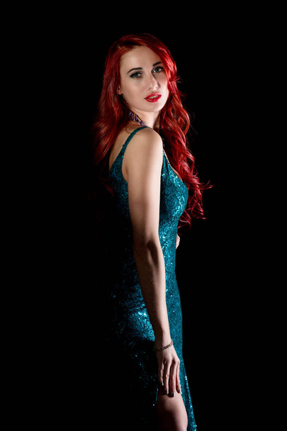 Young redhead sexy woman in blue elegant dress poses in a dark - Fotó, kép
