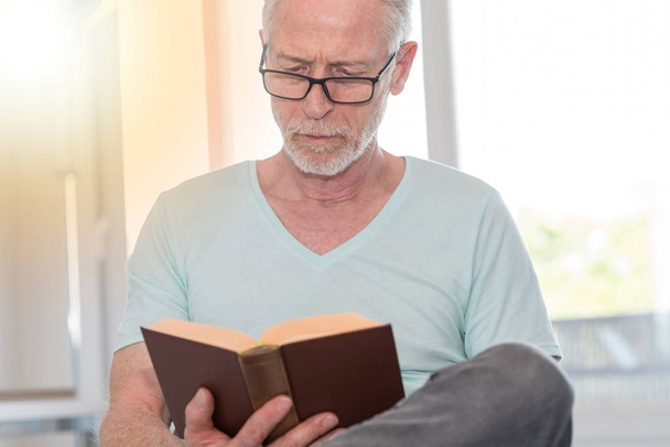 Portrait of mature man reading a book, light effect - Photo, Image
