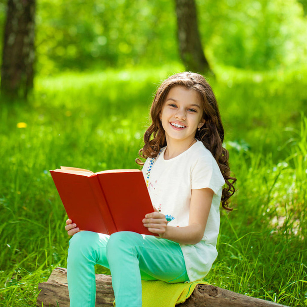Charming little girl in forest with book sitting on tree stump - Foto, immagini