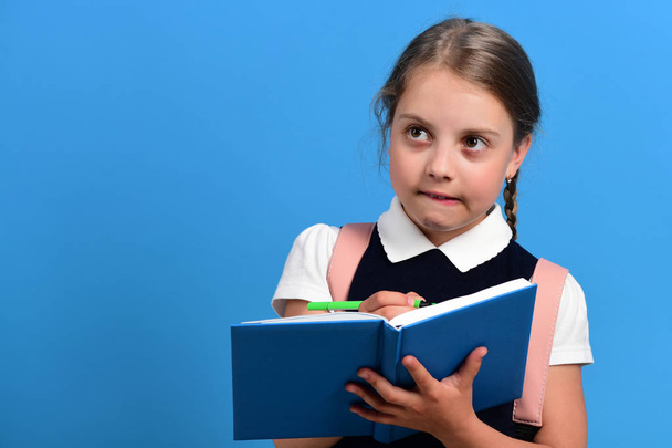 Pupil in school uniform with braid. Girl writes in notebook - Φωτογραφία, εικόνα