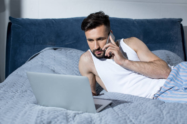 Junger Mann benutzt Gadgets im Bett - Foto, Bild