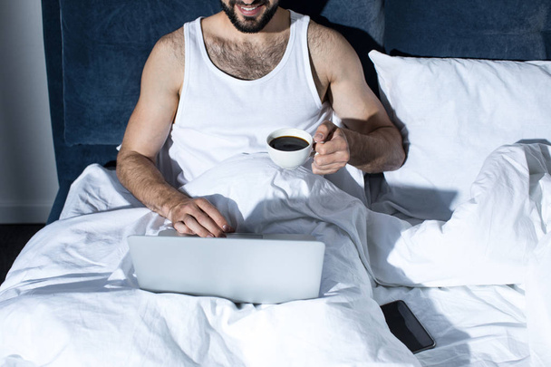 νεαρός άνδρας που χρησιμοποιεί φορητό υπολογιστή στο κρεβάτι - Φωτογραφία, εικόνα