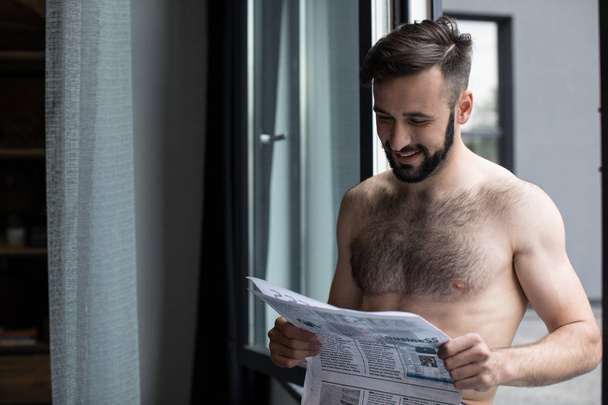 smiling shirtless man reading newspaper  - Fotoğraf, Görsel