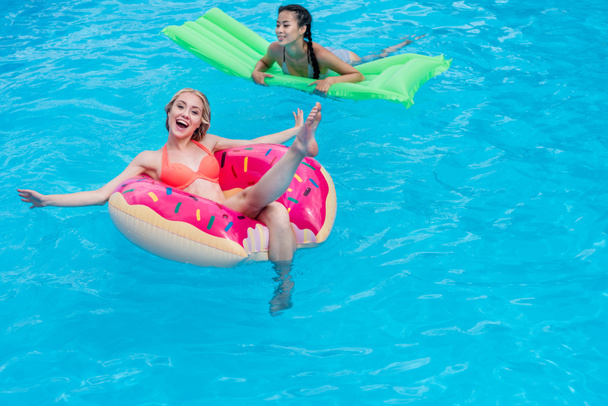 multiethnic women on inflatable mattresses in pool - Photo, Image