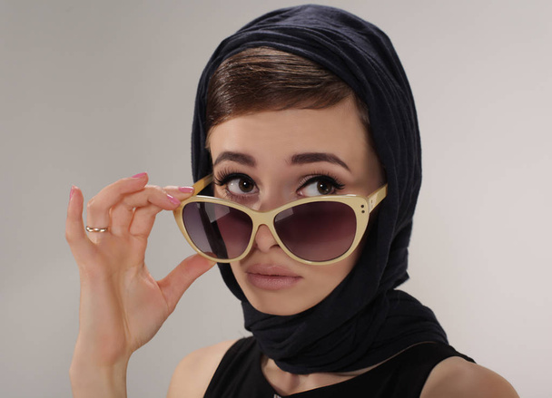 красива жінка в ретро-стилі з навушниками та сонцезахисними окулярами на світлому фоні
 - Фото, зображення