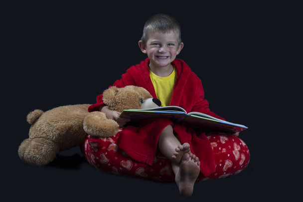 Funny boy with teddy bear reading a book before bed time - 写真・画像
