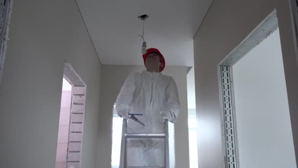 electrician man with helmet climb up on ladder and unscrew light bulb - Footage, Video