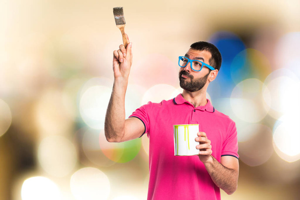 Человек в разноцветной одежде держит горшок с краской
 - Фото, изображение