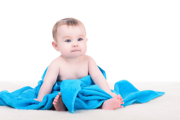 Baby with big blue eyes sitting on the blanket wrapped in blue t - Fotografie, Obrázek