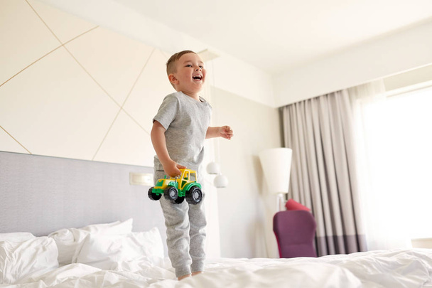happy little boy with toy car on home or hotel bed - Foto, Bild