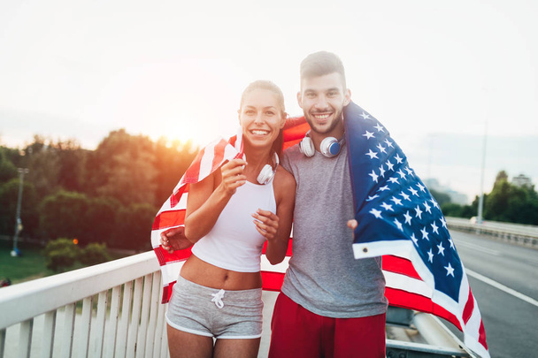 Portrait of attractive fitness couple holding American flag - 写真・画像