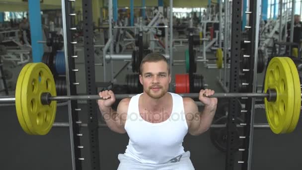 erősítő edzés az edzőteremben. a fickó csinál egy súlyzó zömök. testépítő feladatot súlyzó - Felvétel, videó
