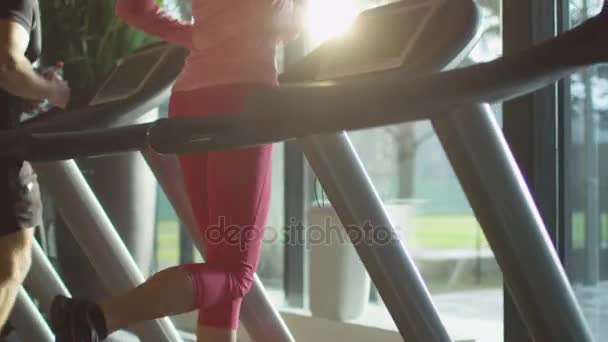 Attractive caucasian girl running on the treadmill in the sport gym with phone and earphones. - Πλάνα, βίντεο