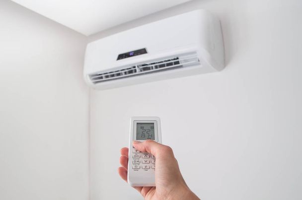 Hand holding remote control for air conditioner on white wall. - Foto, Imagen