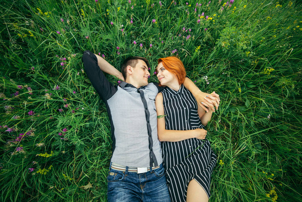 Mladý šťastný nádherný pár muž a žena leží venku na jasného slunečného dne na zeleném trávníku - Fotografie, Obrázek
