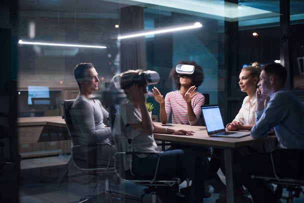 Multiethnic Business team using virtual reality headset in night office meeting  Developers meeting with virtual reality simulator around table in creative office. - 写真・画像