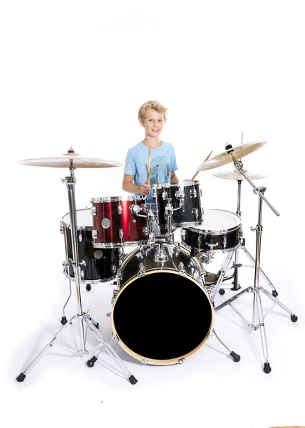 blond teen boy plays drums at drumkit in studio against white ba - Foto, Bild