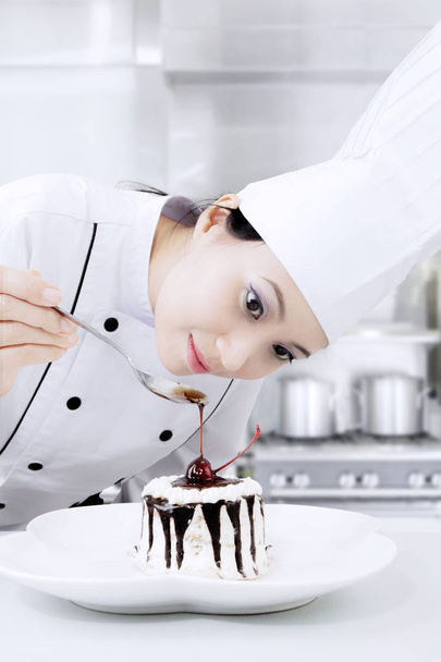 Beautiful female chef decorates a cake - Фото, изображение