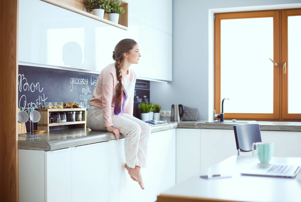 Young woman sitting on table in the kitchen. - Foto, Bild