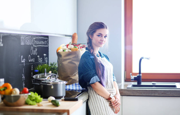 Young woman standing by the stove in the kitchen . - Foto, imagen