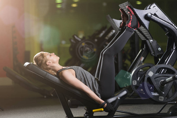 Sportive woman using weights press machine for legs. Gym. - Фото, изображение