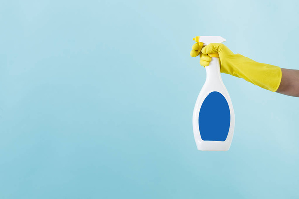 Hand in yellow glove holds spray bottle of liquid detergent on blue background. cleaning - Fotoğraf, Görsel