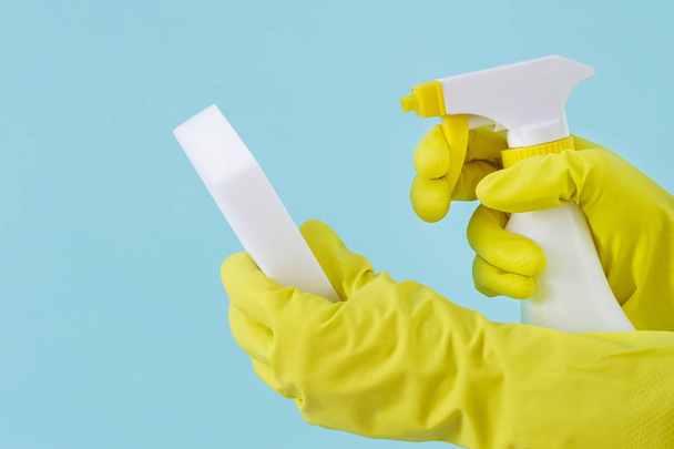 Käsi keltainen käsine pitää spray pullo nestemäistä pesuainetta ja sienellä sinisellä pohjalla. puhdistus
 - Valokuva, kuva
