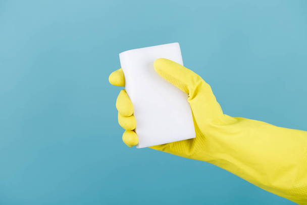 hand  in yellow glove holding sponge on blue background. cleaning - Photo, Image