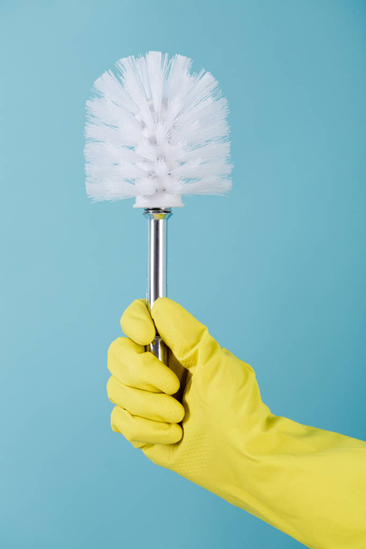 Hand in rubber yellow glove holds brush for toilet on blue background. cleaning. - Foto, immagini