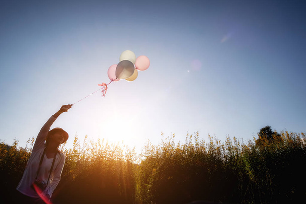 Mädchenhand mit bunten Luftballons auf dem gelben Blumengarten. Relax Konzept. Retro-Filtereffekt, selektiver Fokus - Foto, Bild