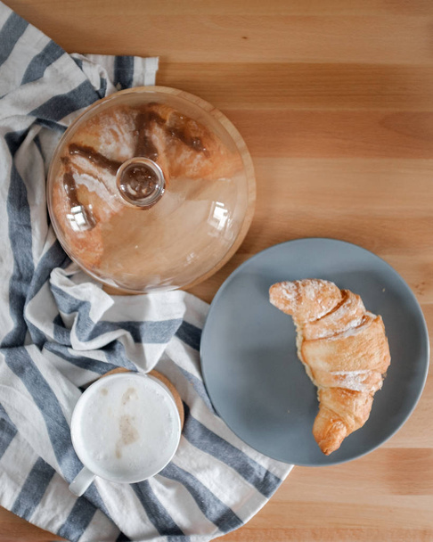 A cup of coffee on a kitchen towel and a croissant on a plate - 写真・画像