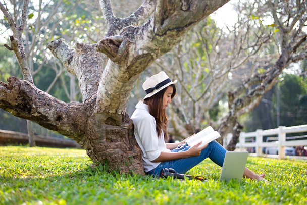 Lifestyle Girl enjoy listening music and reading a book and play laptop on the grass field of the nature park in the morning (greenery tone). Concept lifestyle - Foto, Imagen