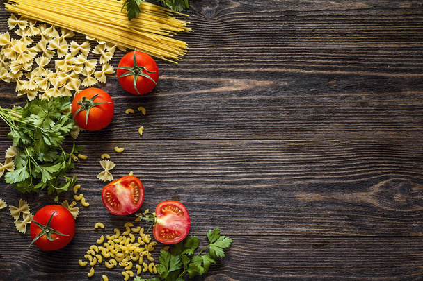 Background with pasta, tomatoes and herb on dark wooden table wi - 写真・画像