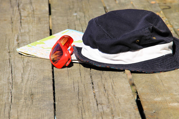 Concepto de viaje. Sombrero, gafas de sol rojas y mapa sobre fondo de madera
 - Foto, imagen