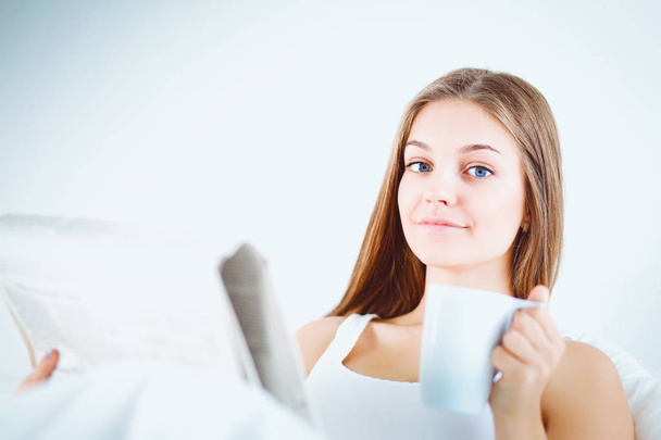 A pretty young woman reading the newspaper in bed and enjoying a cup of tea. - Foto, Bild