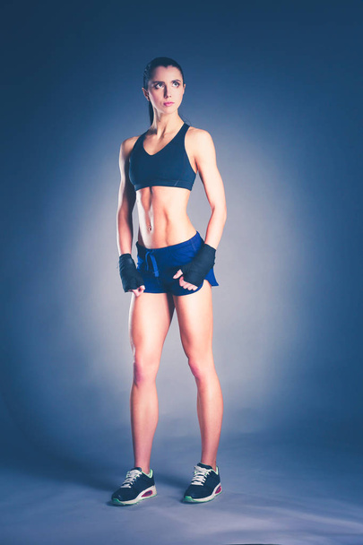 Muscular young woman posing in sportswear against black background. - Foto, afbeelding