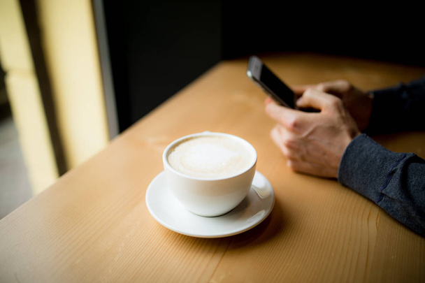 Чоловік вводить смс по телефону під час випивки чашки кави
 - Фото, зображення