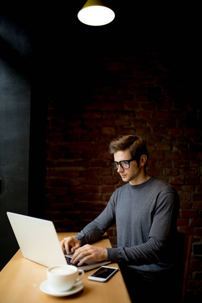 Üzletember használ laptop, a fából készült asztal és egy csésze kávét a kávézóban - Fotó, kép