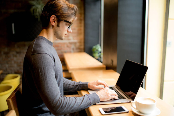 вид сбоку человека с ноутбуком, сидящего в кафе и работающего
 - Фото, изображение