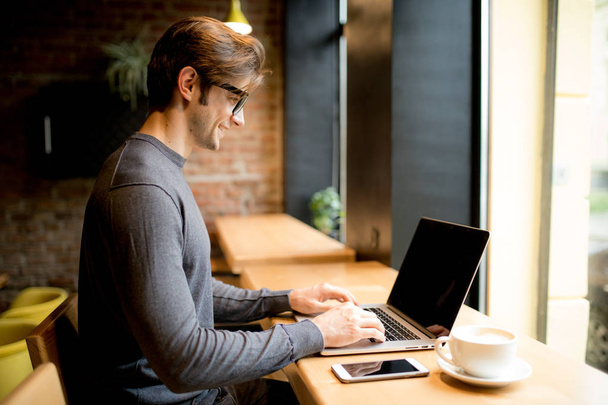 vista lateral del hombre con el ordenador portátil sentado en la cafetería y el trabajo
 - Foto, Imagen