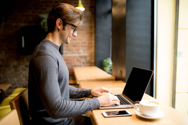 Όμορφος άνδρας σε ένα καφέ με καφέ και φορητό υπολογιστή  - Φωτογραφία, εικόνα