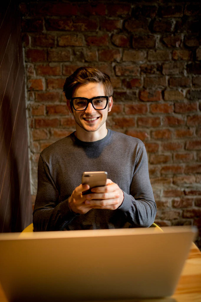 Привабливий чоловік використовує ноутбук, який розмовляє на мобільному телефоні і посміхається під час роботи кав'ярні
 - Фото, зображення