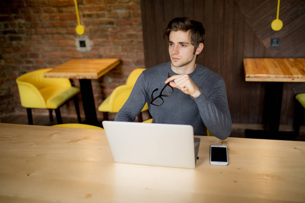 Handsome  man sitting at a cafe table outside working remote with his laptop - Photo, image
