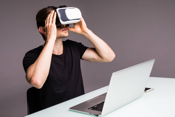 junger gutaussehender Mann sitzt in einem Internetcafé und benutzt ein Virtual-Reality-Headset oder eine Brille. Spielkonzept - Foto, Bild