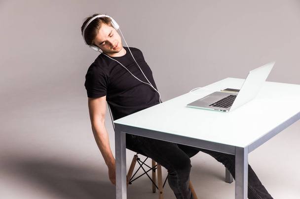 Молодой человек спит в наушниках и работает на ноутбуке на рабочем столе на белом фоне. работа
 - Фото, изображение
